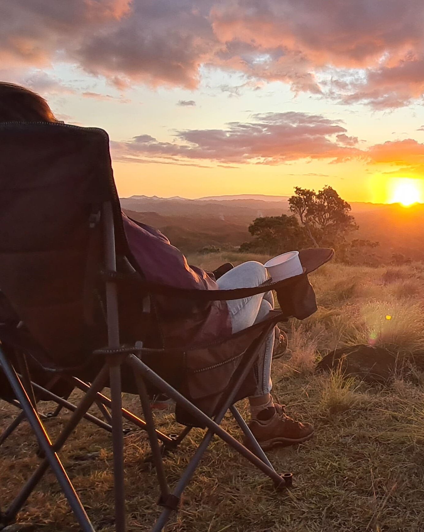 Une personne admire le couché du soleil au point de vue, assis confortablement, en buvant  une boisson chaude